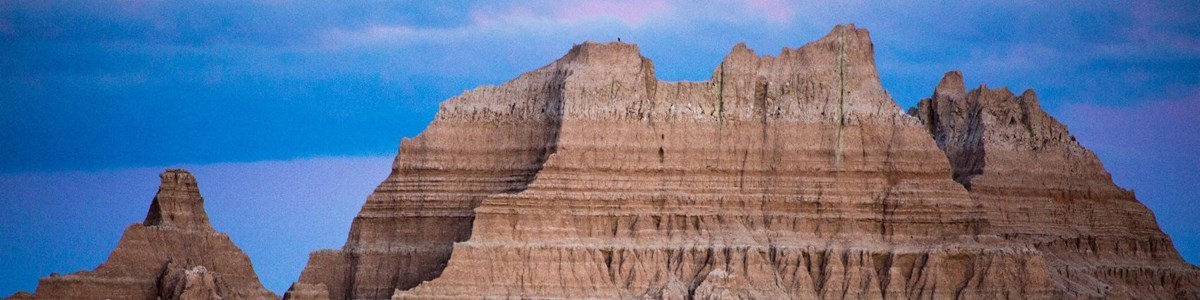 a blue sky with purple clouds sit behind the jagged peaks of badlands formations