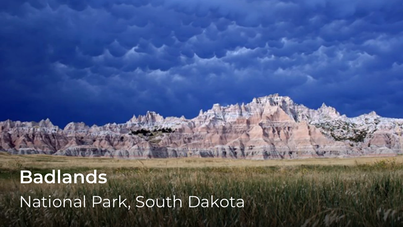 Mountains with a blue, cloudy sky overhead. In the lower left is the word Badlands.