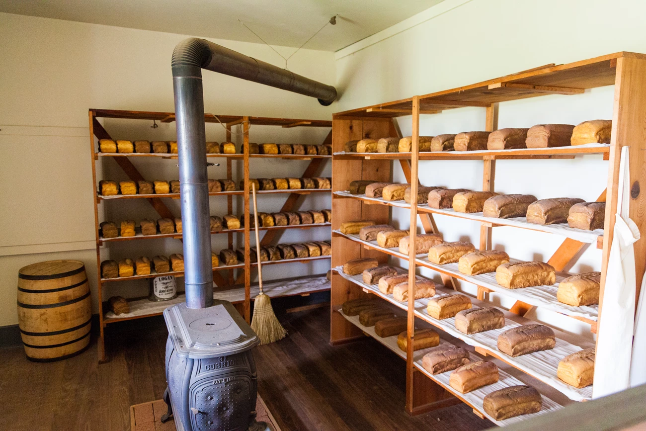 Bakery-20140621_FortLarned_0014 Room with unpainted wood floor, two wooden shelves filled with bread.