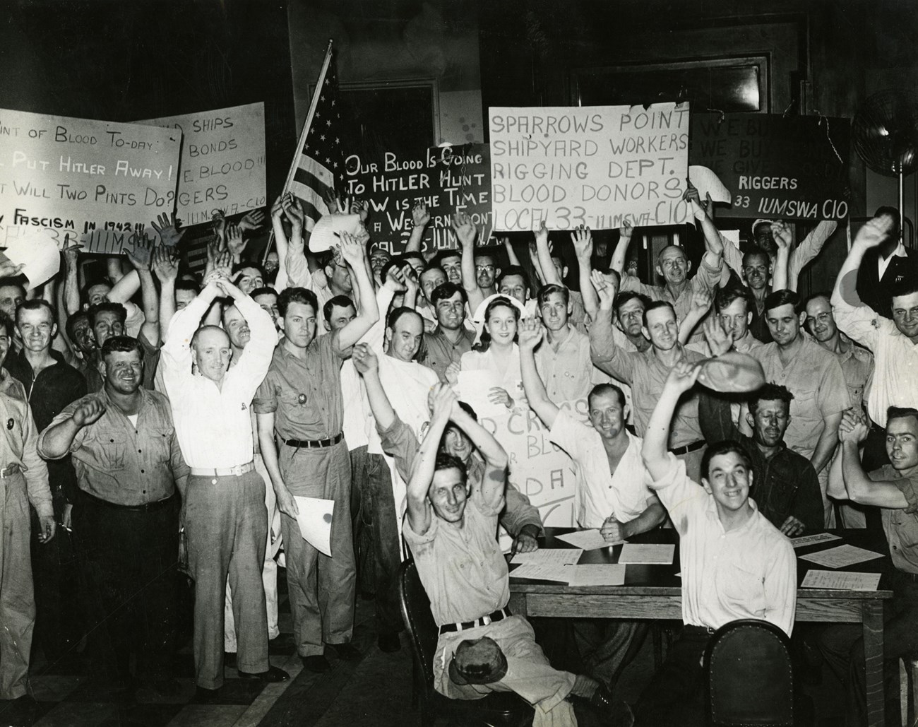 Blood drive at Bethlehem Steel Company, 1942 Black and white photo of large group of men gathered in a room celebrating giving blood during WW2