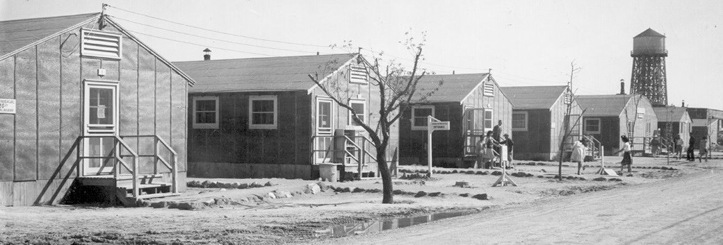 Historic image of a Minidoka residential block. Black and white image of a Minidoka residential block, with a few people standing outside.