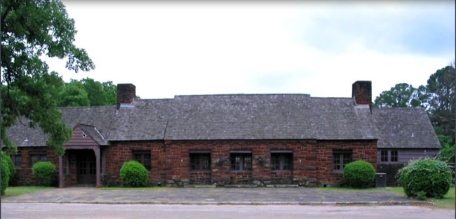 A wide stone cottage with two chimneys on a wood shingled roof.