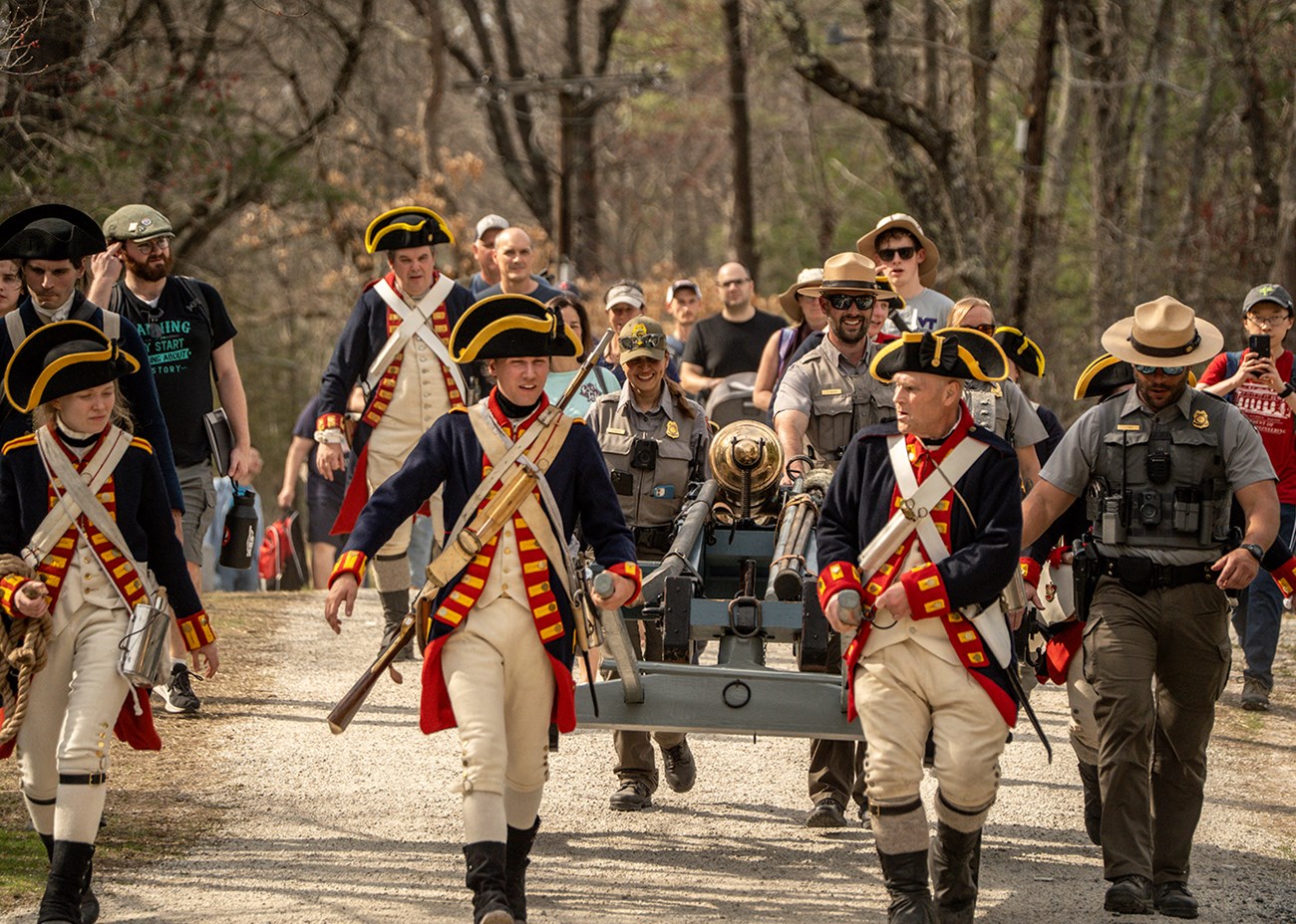 People in historic revolutionary war uniforms marching outside.
