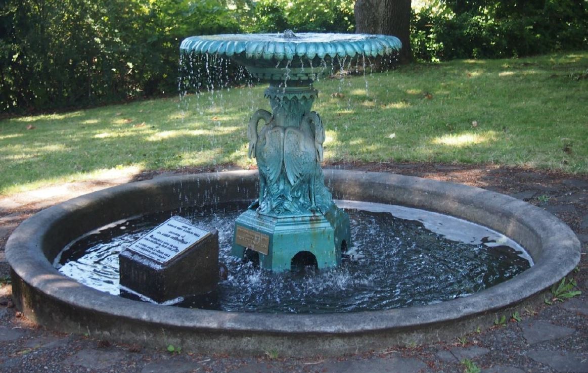 A fountain with a green-blue patina in a shady park.