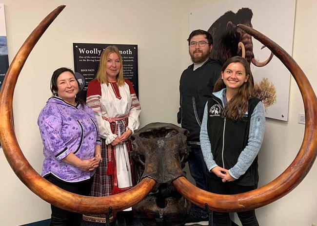 Four people stand by a mammoth fossil.