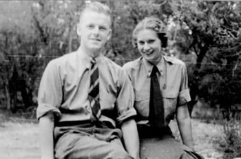 A man and woman wearing NPS uniforms sit next to each other.  Both of them have their shirt sleeves rolled up past their elbows.  They both smile at the camera.