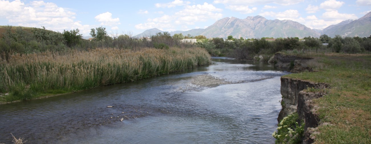 The Jordan River flows near cliff sides with mountains in the distance.