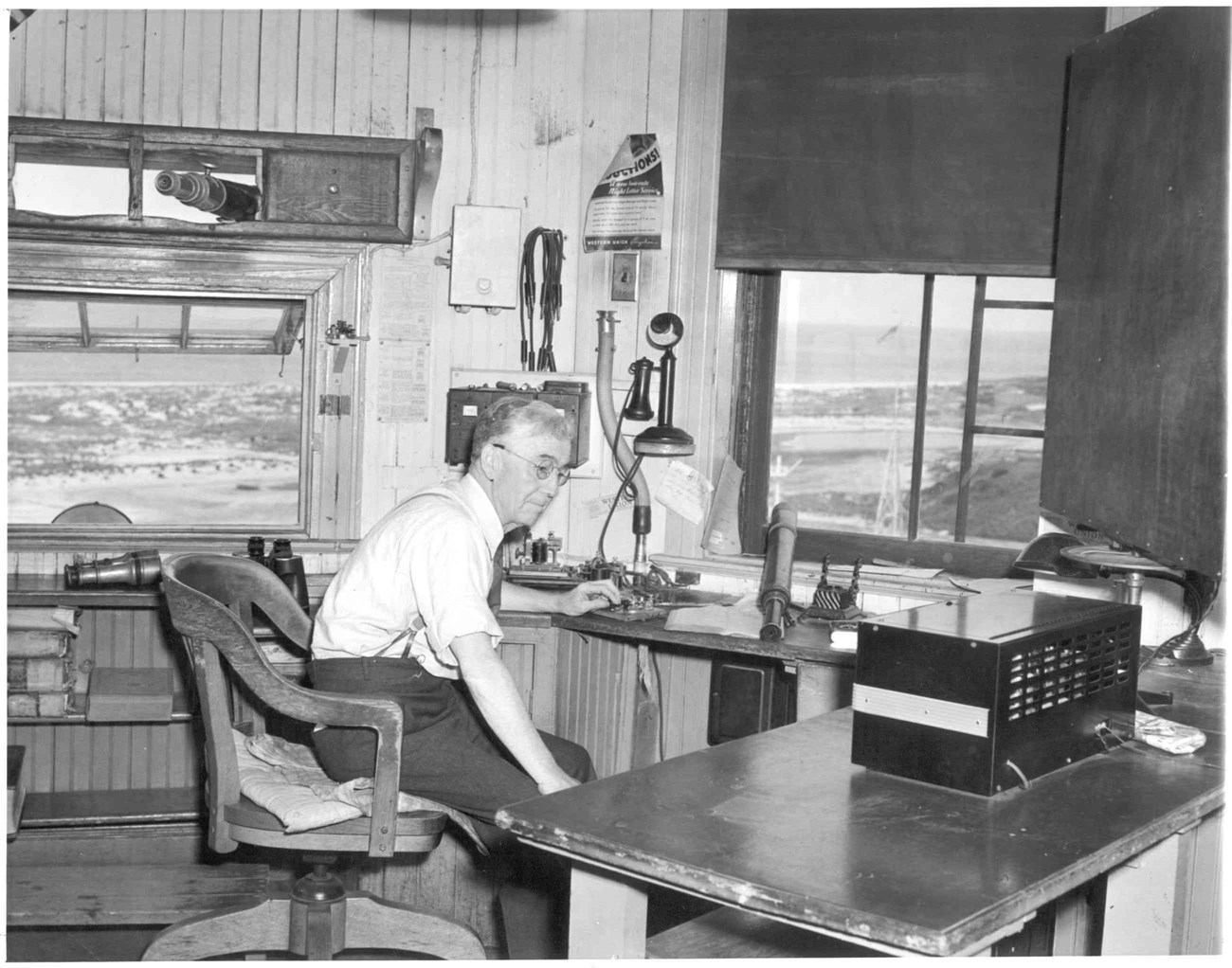 Mr. Gould at work a man sits at a desk with his hand on a morse code device