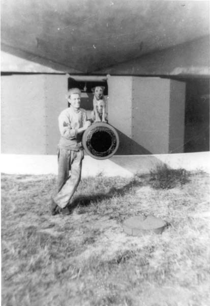 a young man in a military uniform stands next to a military battery with a dog
