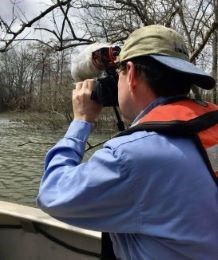 A person looks with binoculars across water