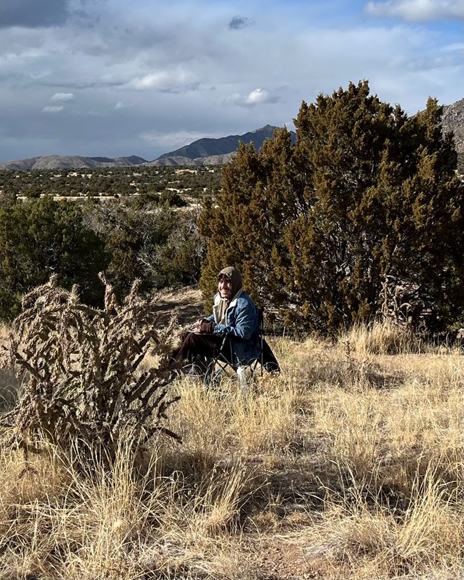 A person sits on a grassy hillside smiling at us