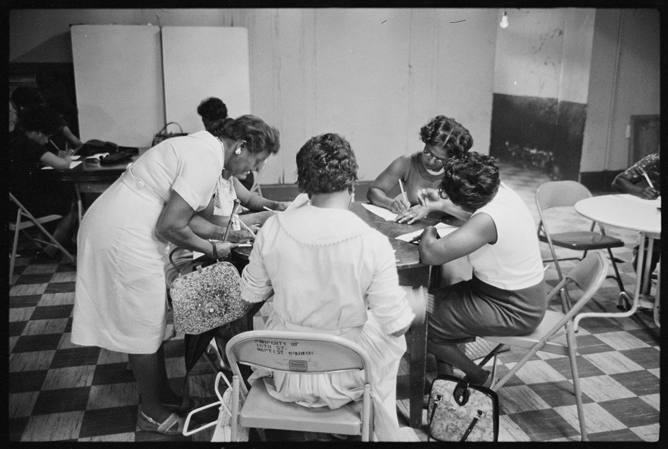Black and white photo of African American women, seated at a table, writing