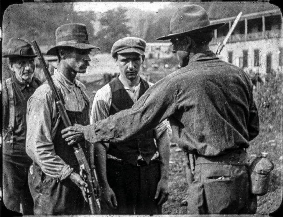 Three men in hats and rough clothing hand rifles over to federal troops wearing uniforms and wide-brimmed hats.