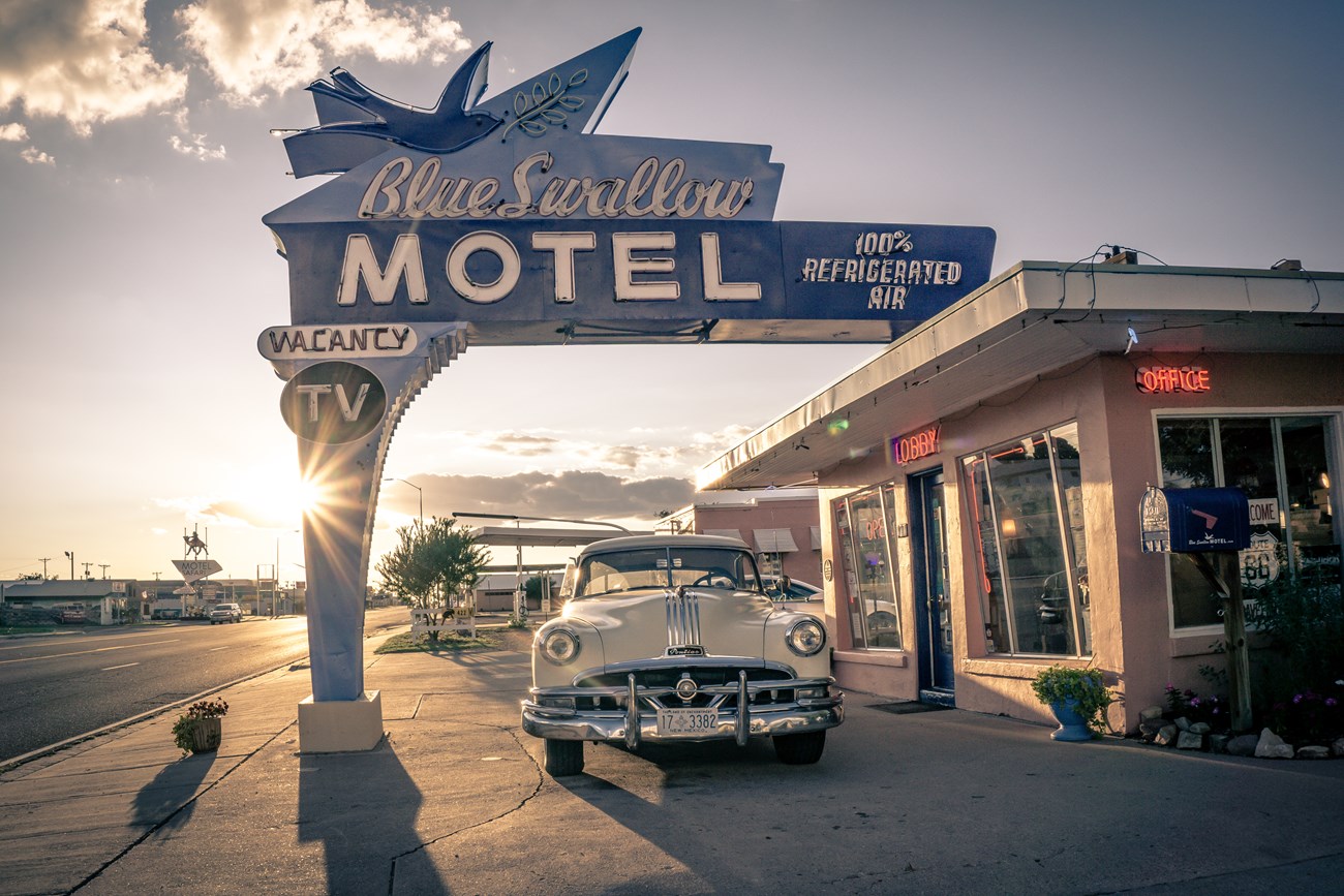 A sign on a street with varying shades of blue that reads "Blue Swallow Motel" with a bird outline on it.