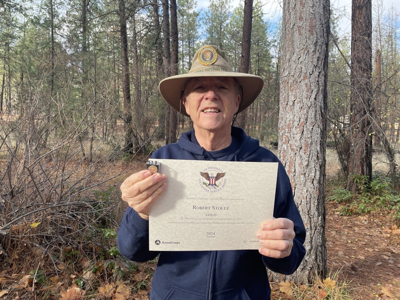 Bob with Certificate Man with a volunteer hat holds up a certificate in front of himself.