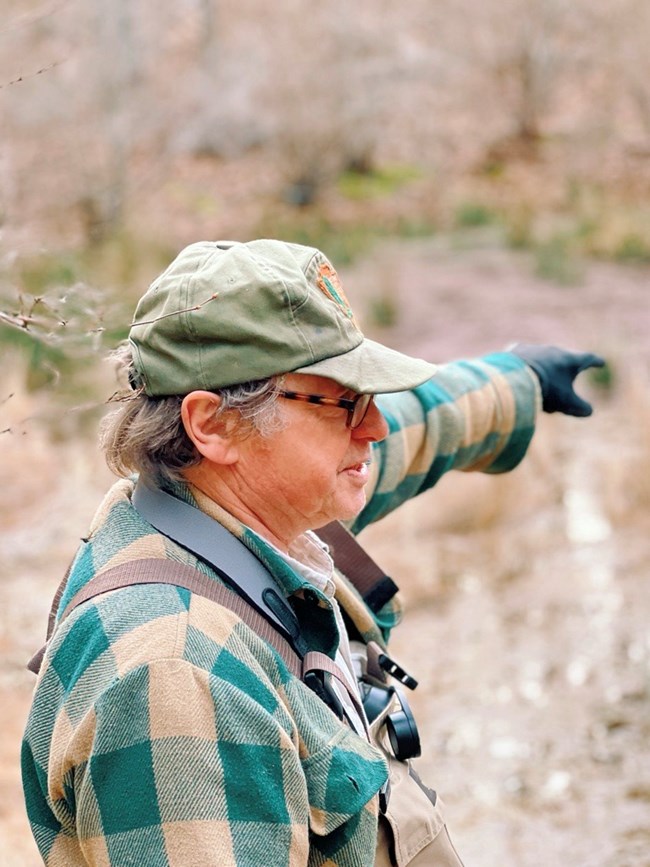 Bob Cook Scientist stands, pointing off into the distance at a vernal pool.
