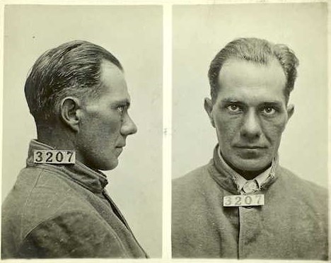 Two photographs of a clean shaven man with slicked back hair. In one he is facing the camera. In the second, he is profile. In both a card displaying number 3207 can be seen attached to his collar.