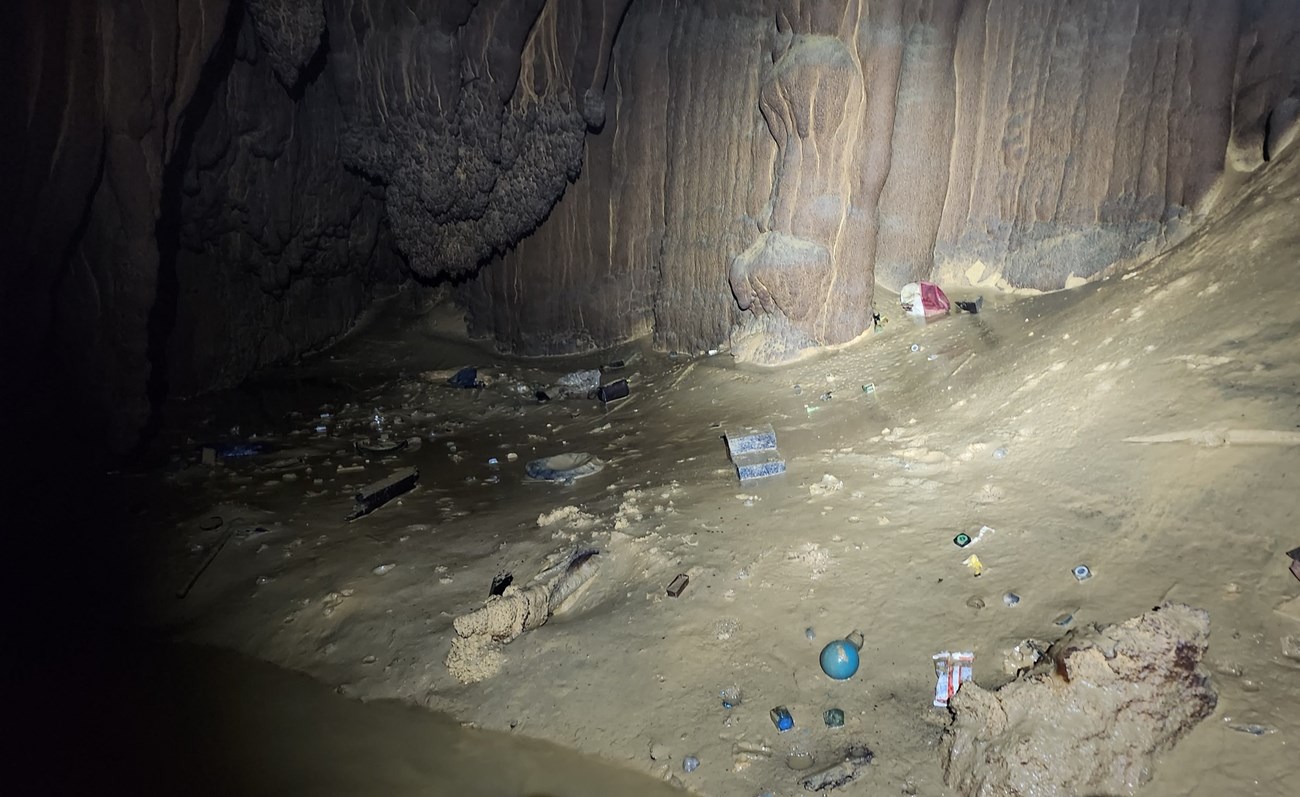Small objects are littered across a muddy floor inside a cave.