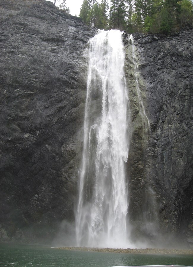 Water tumbles down a steep rock face into a large pool nearby.