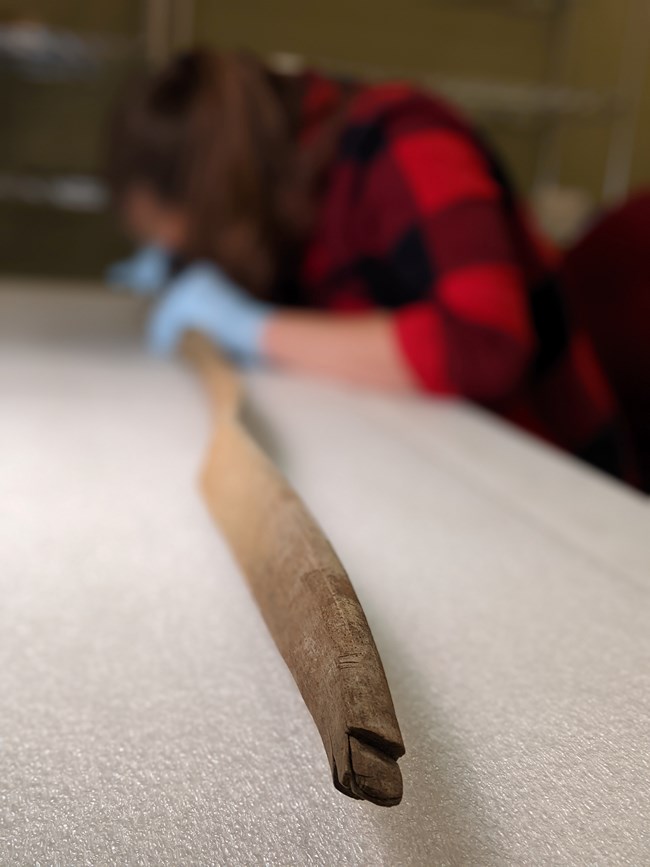a wooden handcrafted archery bow with the notches in focus and a researcher holding the artifact