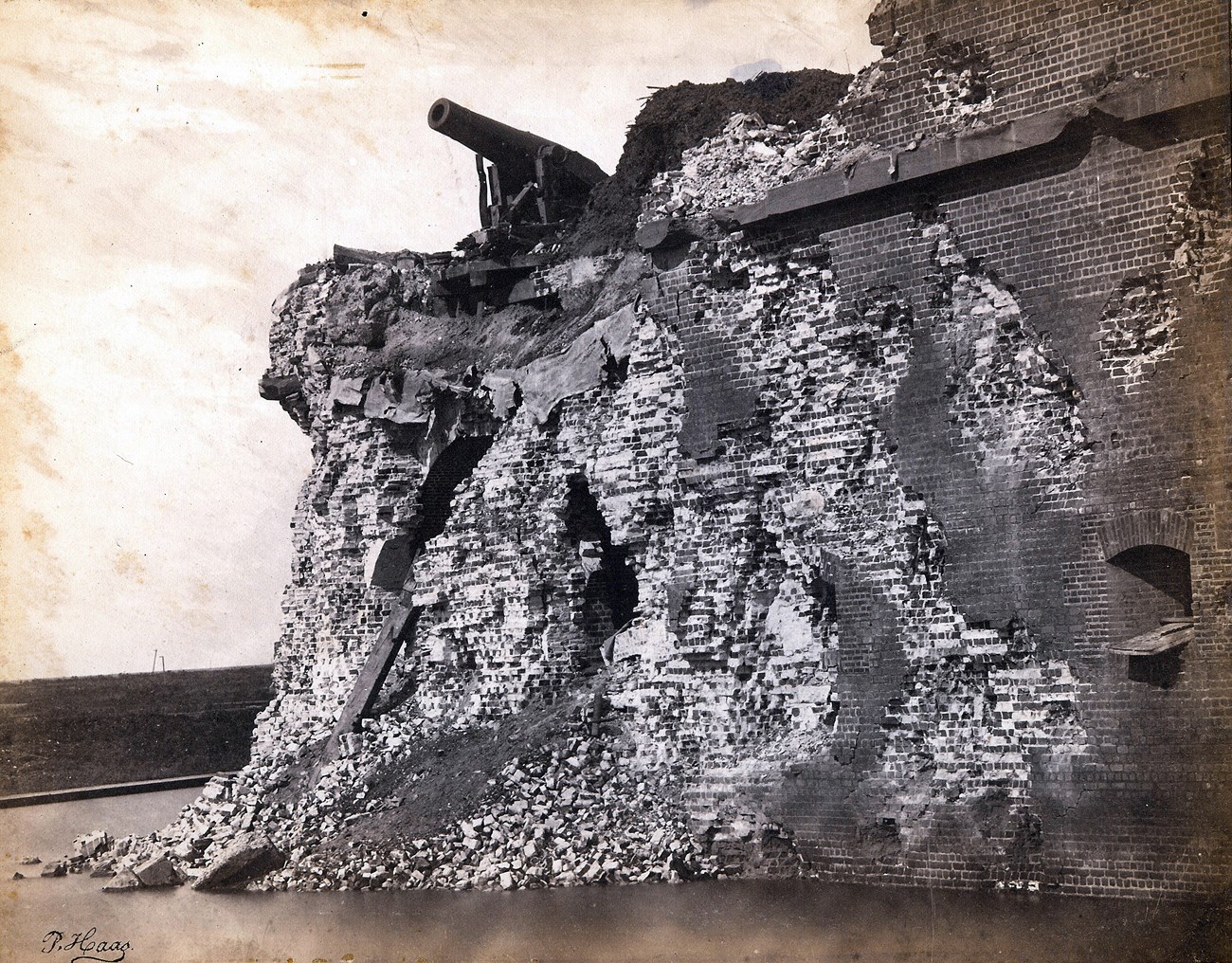 A damage brick wall over a moat with a cannon on top.