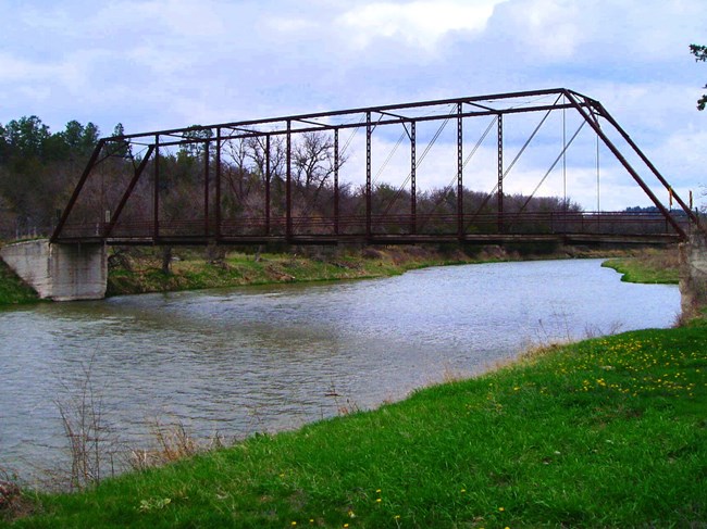 Bridge over a river, concrete supports. Green bank.