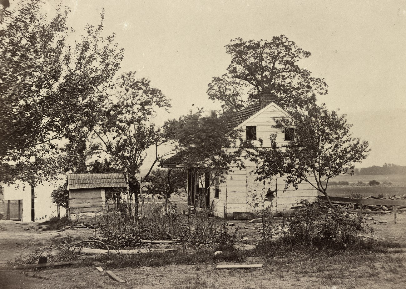 Black and white historical photo of two story white house surrounded by damaged grounds.