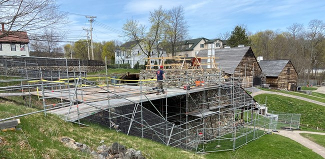 Metal fencing and scaffolding surround a large, stone furnace with shed at the bottom.