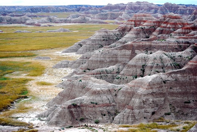 badlands buttes with bright red stripes descend into green prairie grasses below