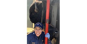 Woman in a navy blue US Public Health Service uniform, smiling at the camera. A captive bison is right behind her.