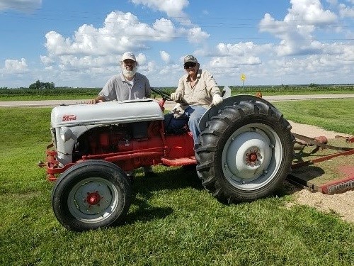 Two people, one seated and another standing, pose for a photo with a tractor.
