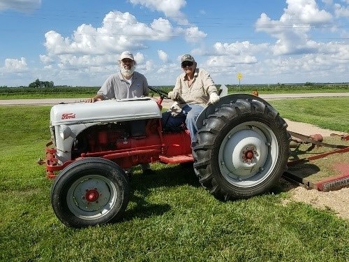 Chris and Lawrence on Tractor Two people, one seated and another standing, pose for a photo with a tractor.