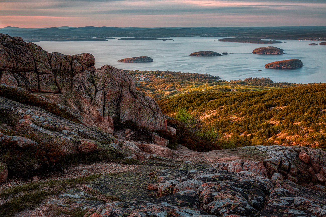 Landscape photo with sloping granite ridgeline at left and numerous round tree-covered islands in an open bay in middle distance