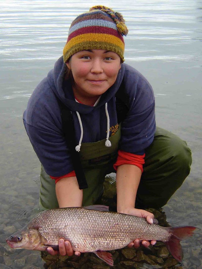 A young woman holds a humpback whitefish she just caught.