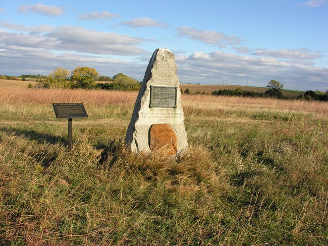 A stone monument grave marker, in a tall grass field.
