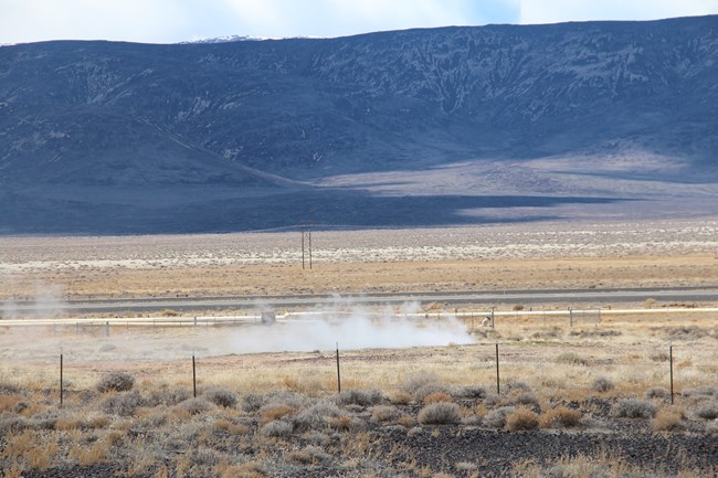 A small, still pond sits in a desert setting void of much vegetation.