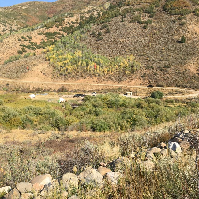 A row of piled rocks, in a field with grass and a distant hill.