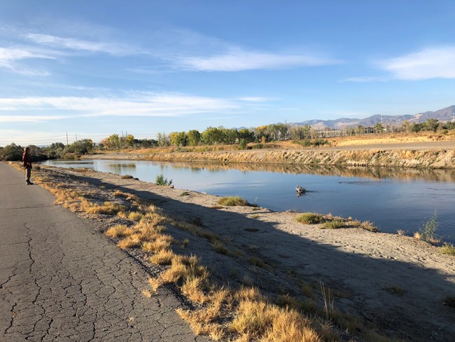 A path runs next to a channelized river in a stark landscape.