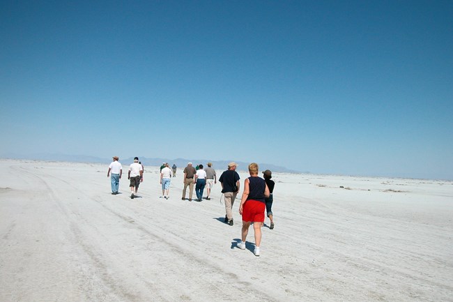 lt= A group of people walk on an large salt flat that extends for miles.