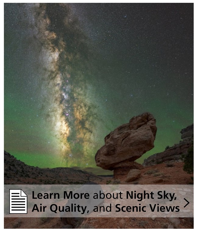 Click here to learn more! A greenish-black sky with scattered stars and the Milky Way, as well as a balancing boulder in the foreground.