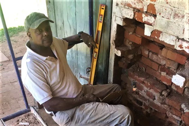 A mason sitting next to an exposed interior brick wall