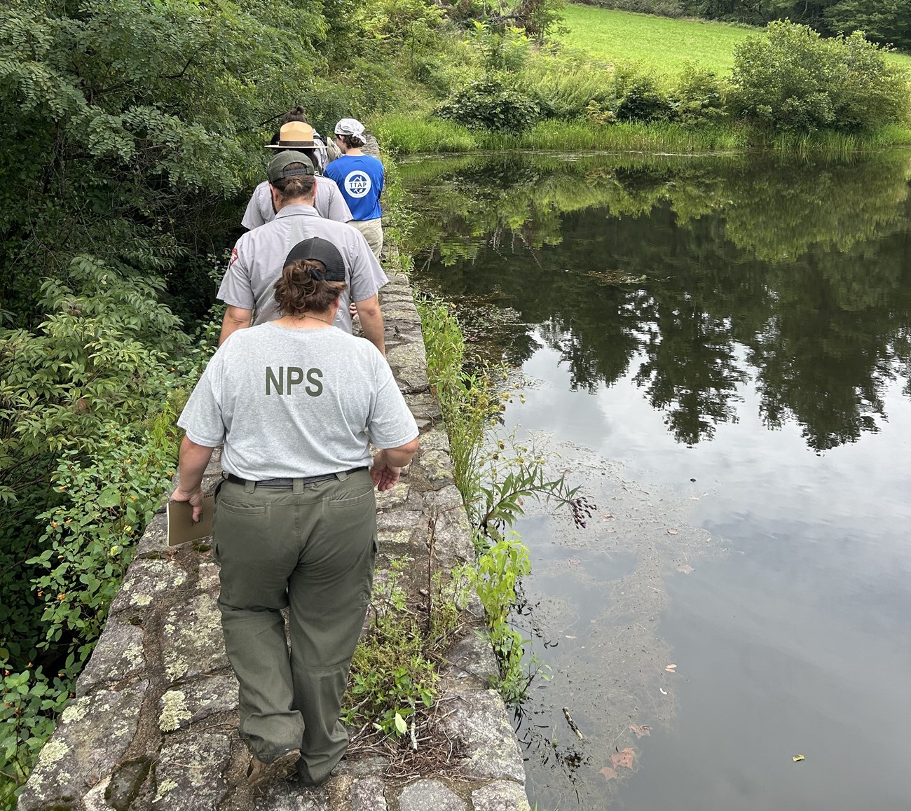 People walking across a stone bridge next to pond