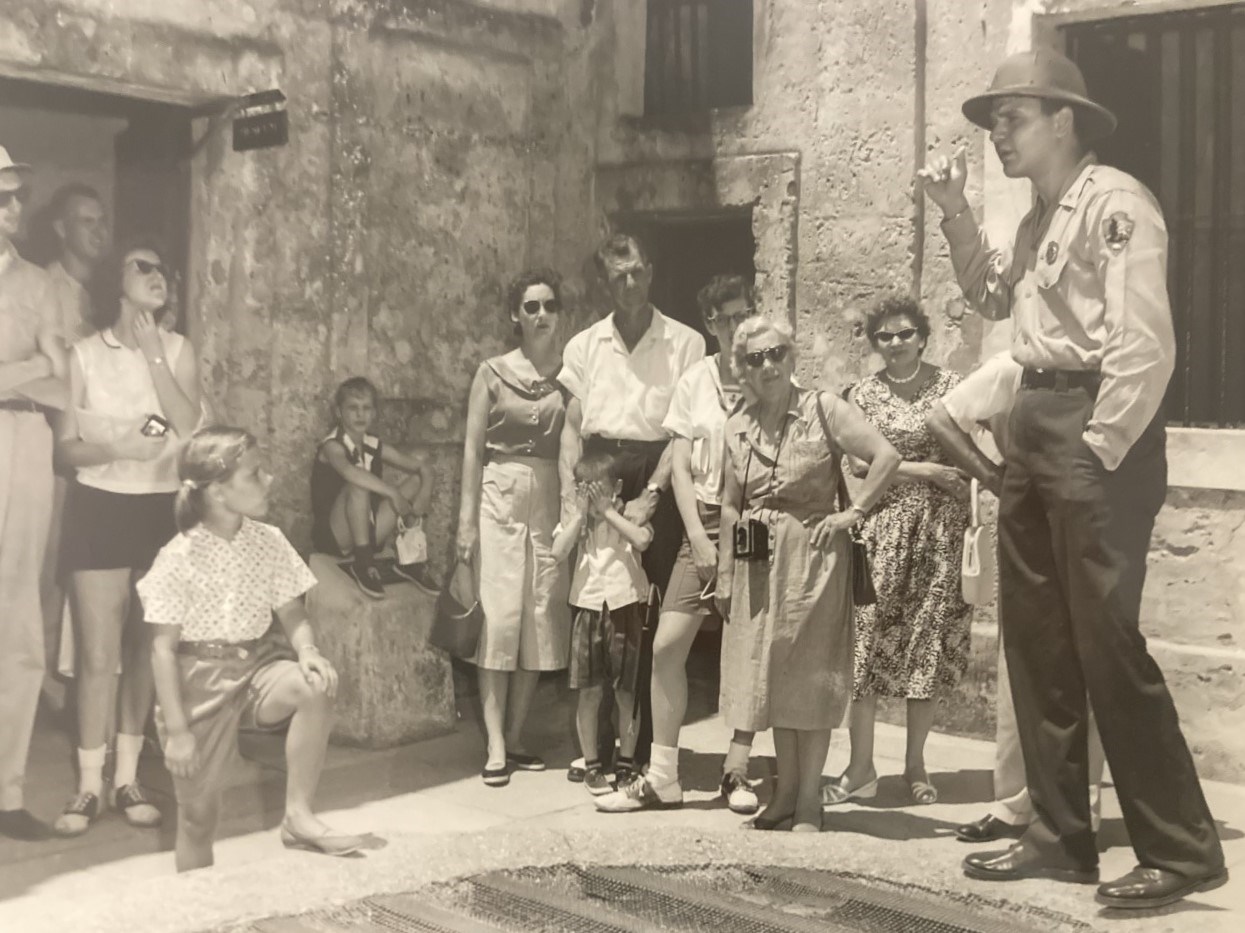 Ranger wearing a sun helmet with his uniform stands talking to a group of visitors.