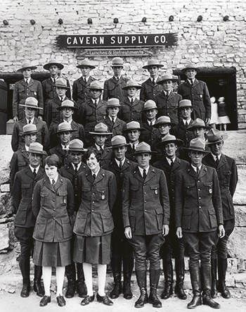 Five rows of uniformed Rangers stand in front of a stone building with a wooden sign that reads Cavern Supply Co.