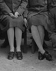 Close up of two women sitting.  The focus on their knees down show the color of their stockings and oxford style shoes.
