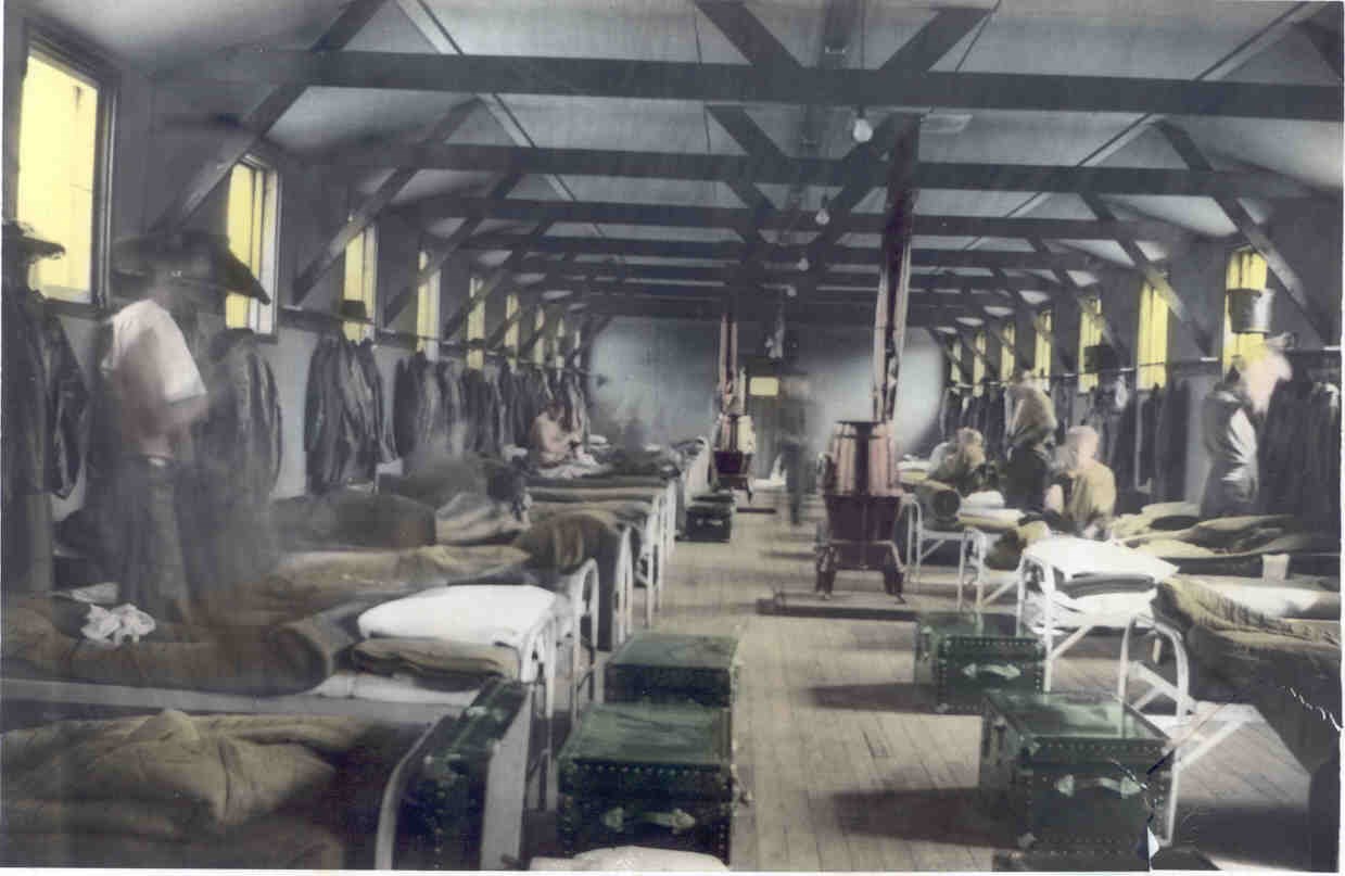 beds lined up against the interior wall of a barrack with trunks in front