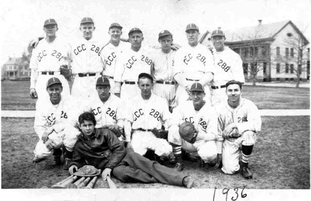 13 men in baseball uniforms pose on a grassy lawn