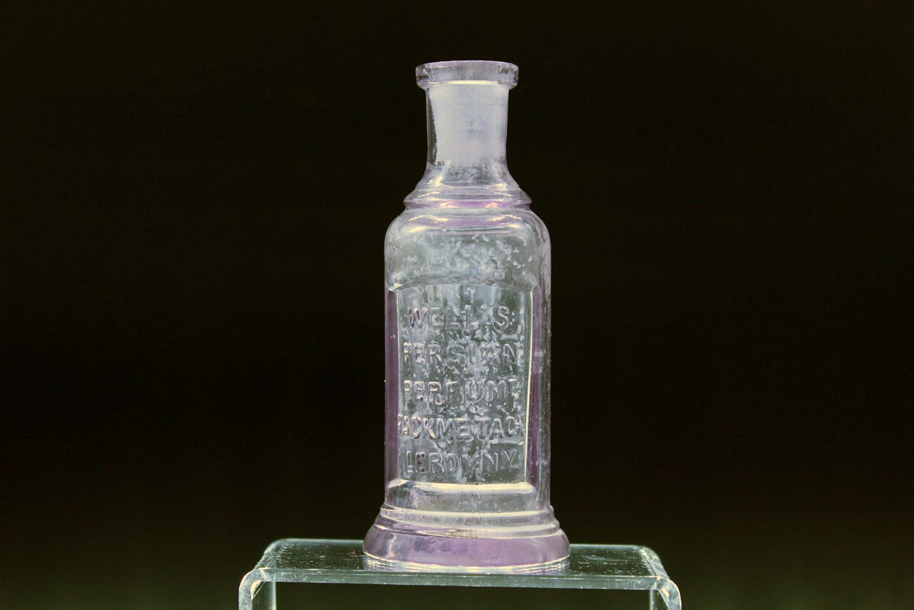 Perfume Bottle Small glass bottle with inscription sits on acrylic stand.