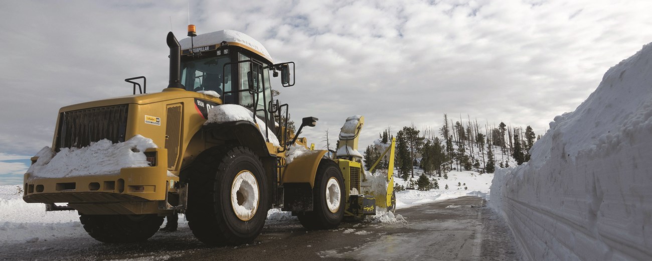 A large yellow tractor parked along a road lined with tall banks of snow