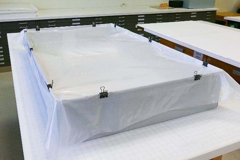 Polyethylene sheet secured with binder clips over container.